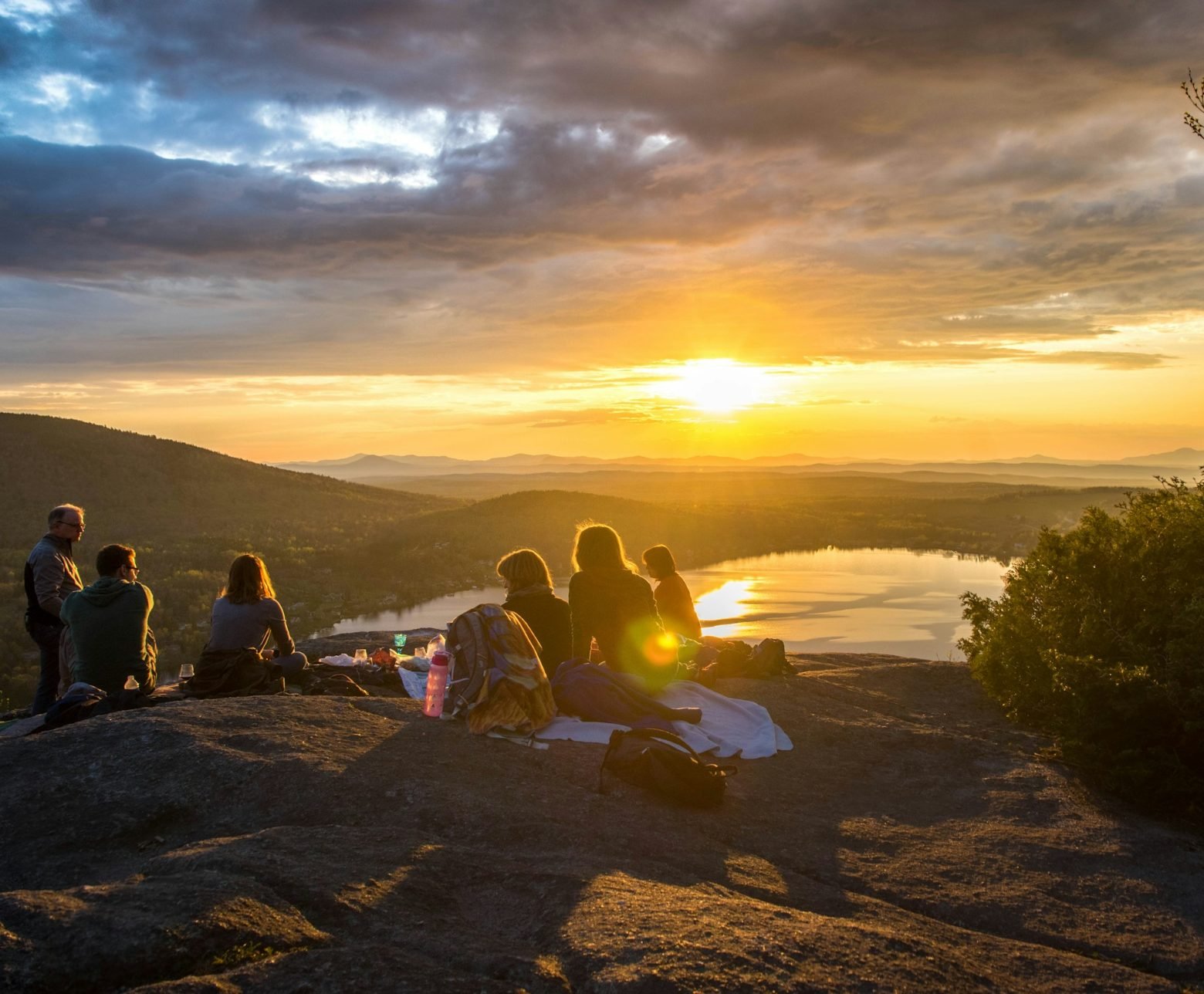 Un grup de persones al cim d'una muntanya mirant la posta de sol sobre un llac