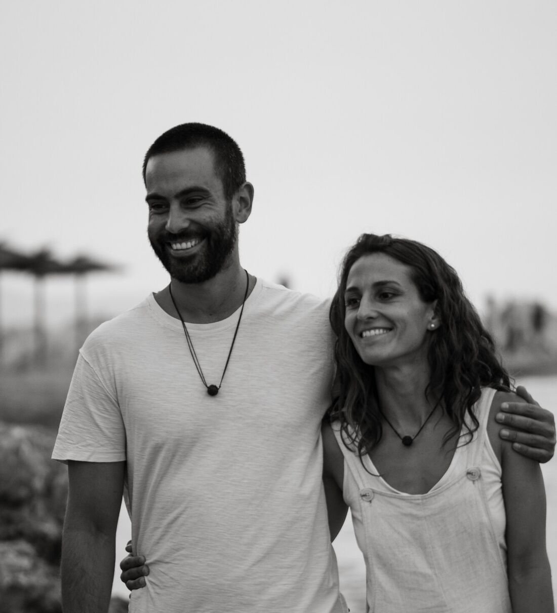 Sergi Colomer i Elisabeth del Río caminant junts i somrients a la vora del mar, en blanc i negre